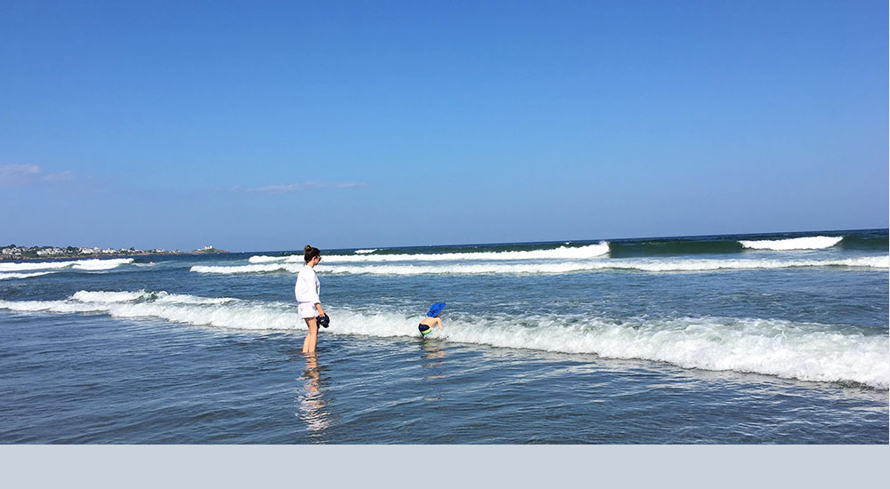 Child playing in the water with mother looking on.